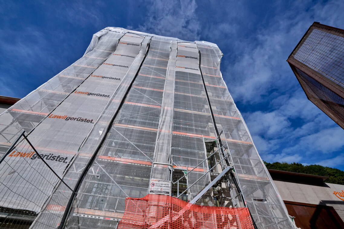 Weihnachtsschmuck verziert ein Baustellengitter, im Hintergrund ein Mehrfamilienhaus